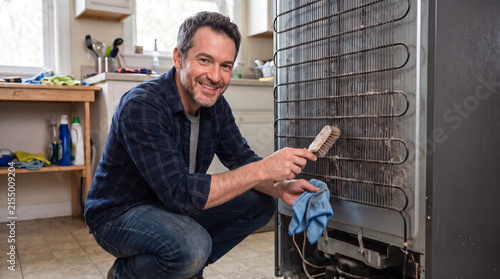 Man cleaning dirty refrigerator coils in a kitchen setting  