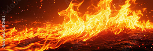 Intense orange and yellow flames spread across a charred textured surface, against a dark background.
