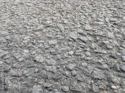 Fotografie Close-up of a heavily worn asphalt road surface with exposed coarse aggregate and irregular gravel, showing deterioration and rough pavement texture