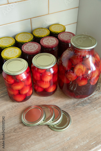 Homemade canned preserves in glass jars with metal lids and additional canning lids on a wooden table, traditional food preservation concept.