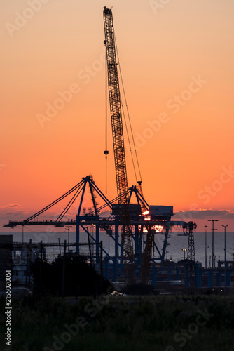 Sunrise though cranes. Construction crane and container cranes in front of the sunrise.