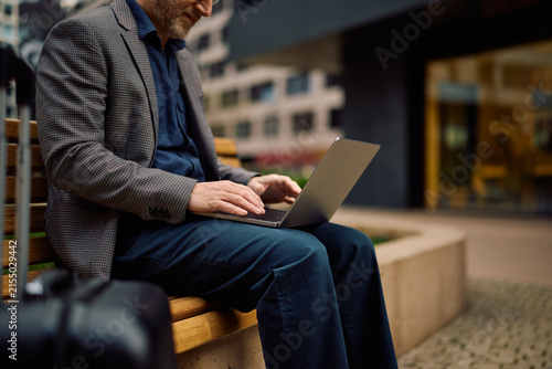 Unrecognizable business traveler surfing the net on laptop outdoors.