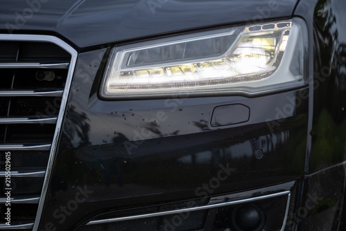 Close-Up Of Luxury Black Car Front Headlight And Chrome Grille With Illuminated LED Lighting