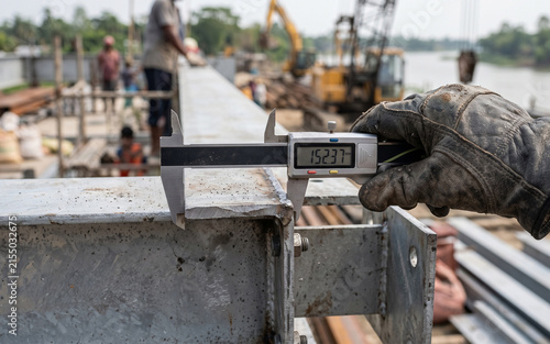 Worker using digital caliper to measure steel beam on construction site