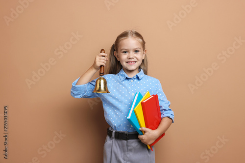 Pretty little girl with school bell and books on color background