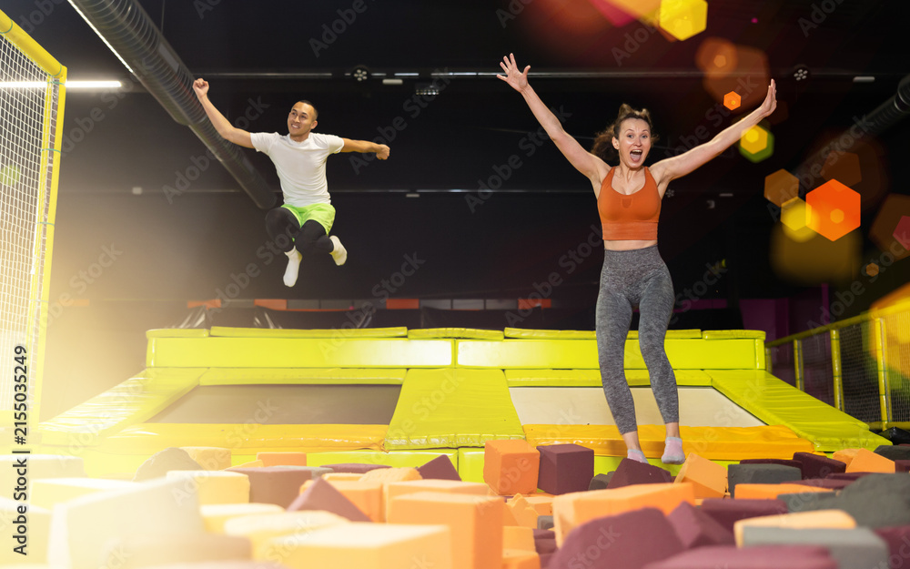 Fototapeta premium Happy excited middle-aged woman playfully jumping into colorful foam cube pit at lively indoor trampoline park