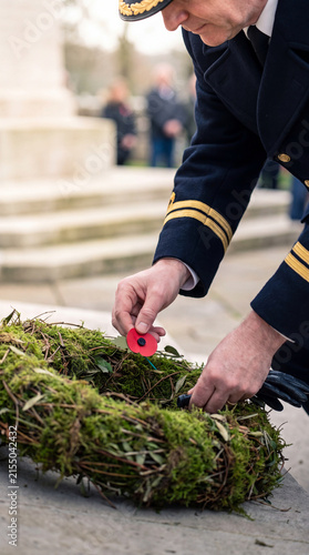 A solemn moment as a person in uniform places a red poppy onto a green wreath at a monument.