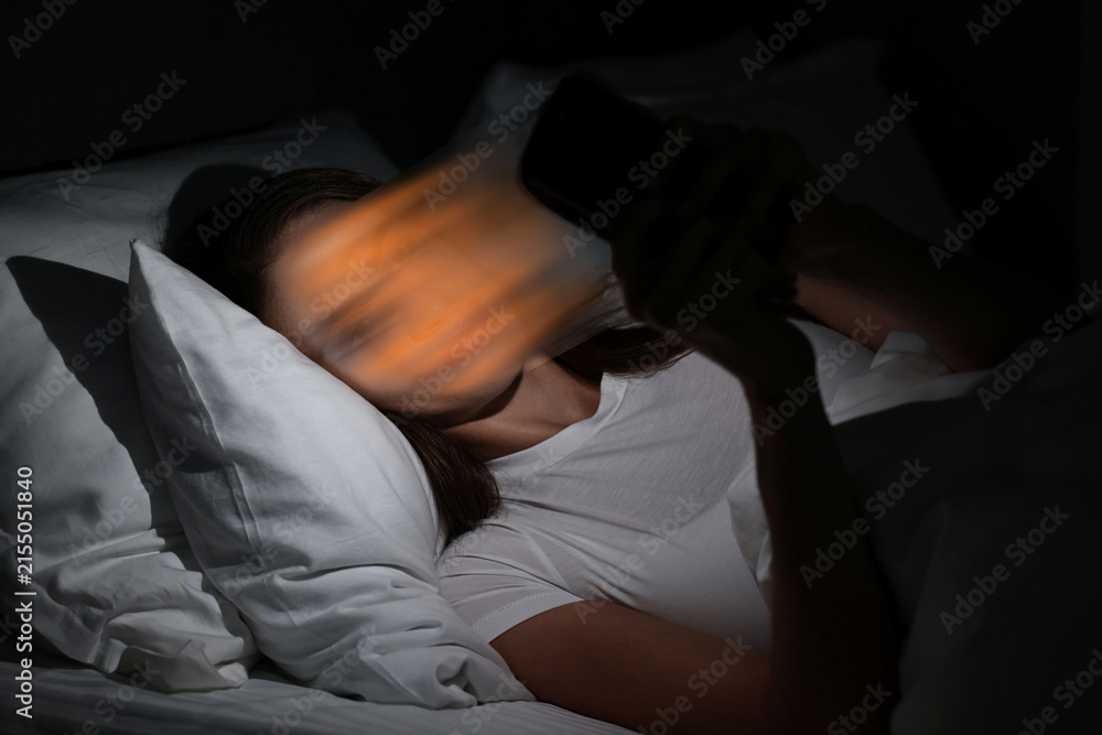 Fototapeta premium Social media addiction. Woman using smartphone in bed at night. Depiction of user being dragged into digital world