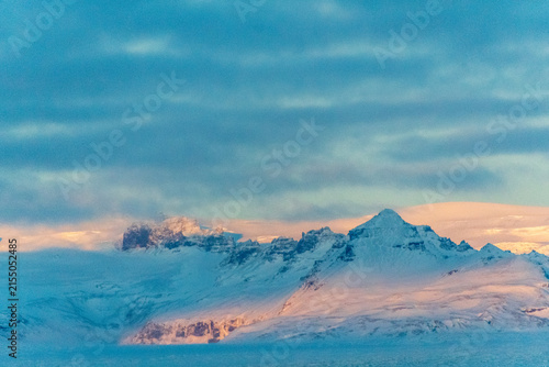 Icebergs and huge chunks for green-blueish ice fill Jokulsarlon Glacier lagoon, as the golden hour sunlight of the early morning casts a beautiful warm glow over the glacier-filled national park in