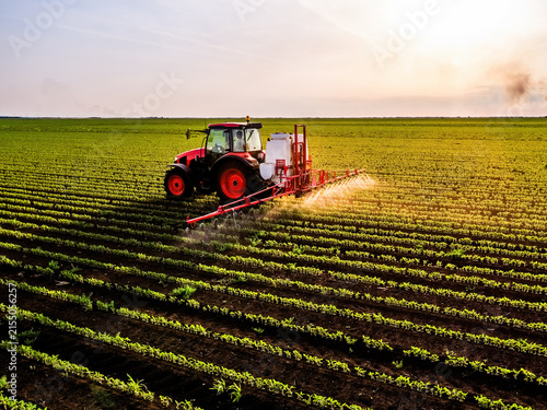 Farmer spraying soybean field with tractor at sunset