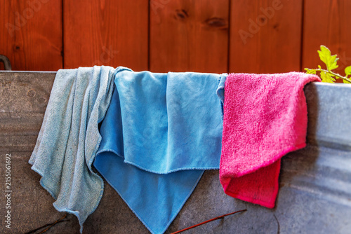 Colorful reusable microfiber cleaning cloths and towels draped over the rim of a galvanized metal tub 
