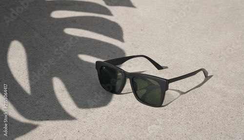Stylish sunglasses with shadows on a light surface