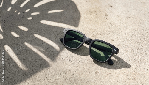 Stylish sunglasses with shadows on a light surface