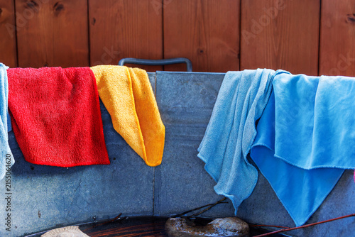 Colorful reusable microfiber cleaning cloths and towels draped over the rim of a galvanized metal tub