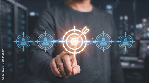 Businessman pointing at glowing digital target icon in server room representing customer acquisition, audience targeting, and business goals