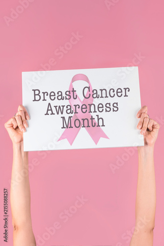 Female hands holding white sign for Breast Cancer Awareness Month on solid pink background