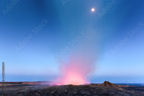 View of the glowing lava lake of Erta Ale volcano under a twilight sky with a visible moon.