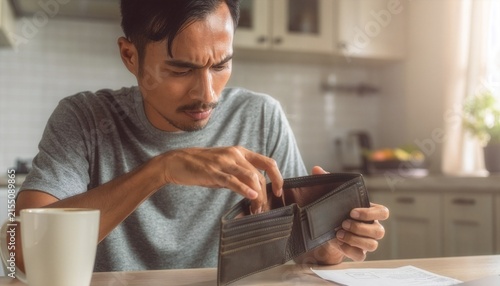 Close-up of a person checking an empty wallet at a kitchen table.
