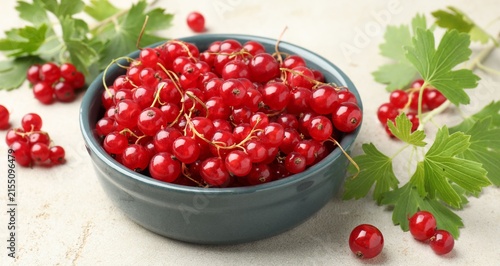Fotografía Fresh red currants in bowl and green leaves on light textured table, closeup