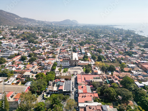Ajijic, Jalisco, Mexico: drone view of town center, colorful buildings, plaza, trees, Lake Chapala, and mountains on a sunny day