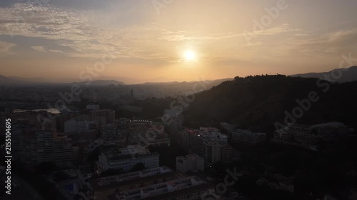 Aerial view of Malaga bullring (Plaza de Toros de la Malagueta) illuminated at sunset. Cinematic drone shot of the coastal arena, Mediterranean sea, and city skyline during golden hour.
