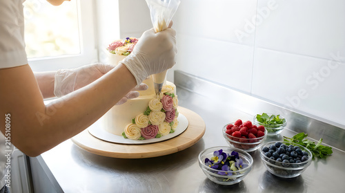 Professional pastry chef decorating a delicious layered cake with fresh berries in a bright modern kitchen