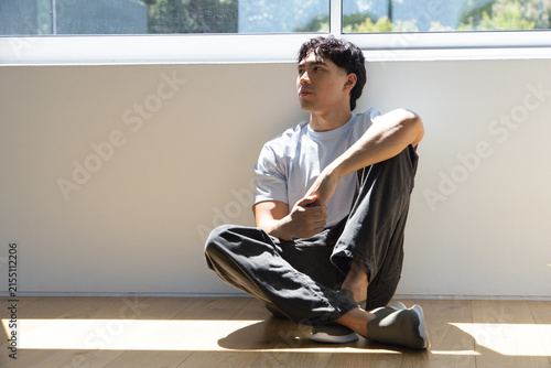 Foto Adult man sitting on wood floor at home by window, T-shirt, showing shoe and sun