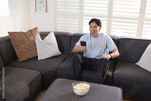 Принти на полотні Asian man sitting on gray sectional sofa wearing light blue tee holding smartpho