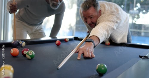 Diverse men playing pool on blue-felt during casual game, one lining up shot, striking cue ball