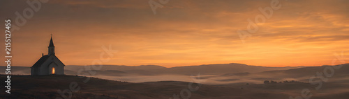 Serene chapel stands tranquil valley sunrise, surrounded by misty hills and warm, golden sky. peaceful atmosphere evokes sense of calm