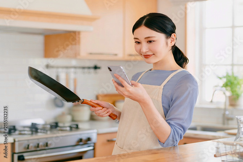 スマホを参考にしがらフライパンを振る主婦