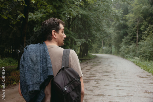 Side view of male tourist with backpack walking on dirt road in green forest