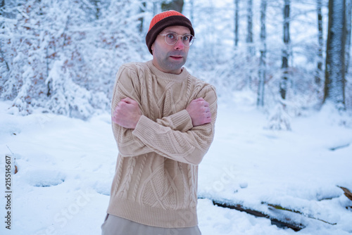 Young man in beanie and sweater shivers in snowy forest, looking lost and cold, survival struggle, winter danger, hypothermia risk, urgency rescue, Frozen and alone, freezing outdoors, lost person