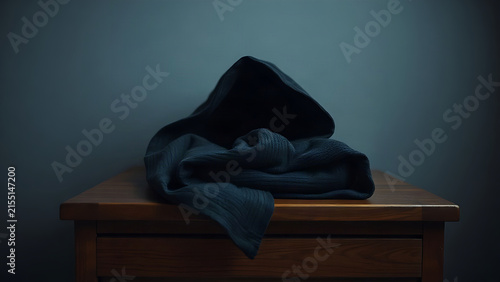 A dark hooded robe folded on a wooden chest with side lighting.