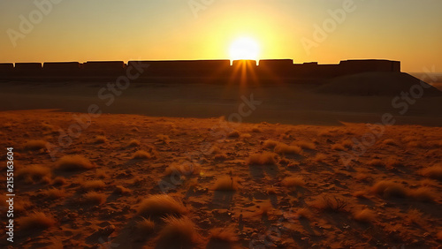 A vast dry plain at sunset with the long shadow of an ancient mud-brick wall.