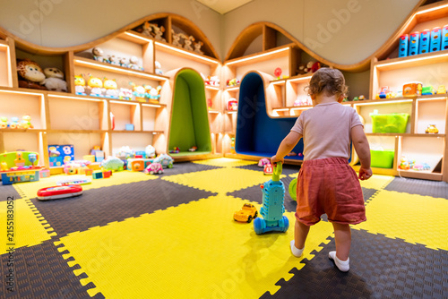 фотографія Toddler playing with a colorful vacuum toy in a vibrant playroom with shelves fu