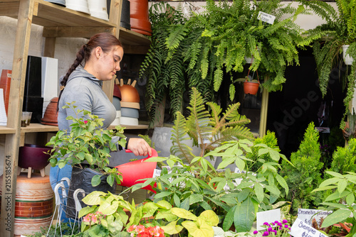 Woman tending to a variety of plants with a red watering can in a lively plant shop