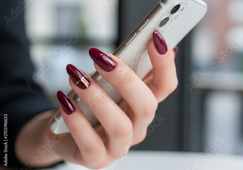 Woman hand with elegant burgundy manicure holding white smartphone