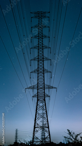 Cuadro en lienzo Perfectly symmetrical vertical view of a high voltage transmission tower silhouette against a cinematic starry night sky with a deep blue gradient