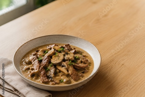 Beef Stroganoff in a Bowl: A hearty serving of Beef Stroganoff, featuring tender beef strips and mushrooms in a creamy sauce, presented in a rustic bowl on a wooden table.