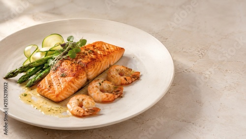 Gourmet Salmon and Shrimp Dinner: A perfectly grilled salmon fillet and succulent shrimp are artfully plated with tender asparagus spears and thinly sliced cucumber, drizzled with a light herb sauce.