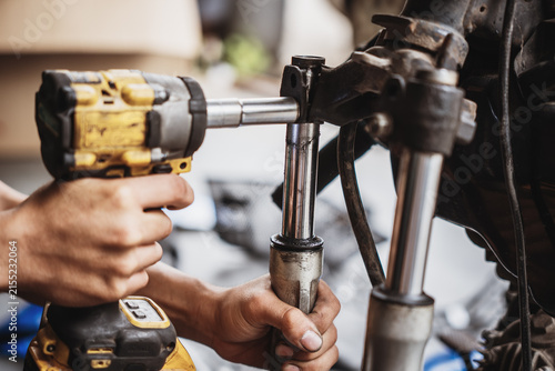 Mechanic using cordless impact wrench to disassemble motorcycle front fork and triple tree assembly