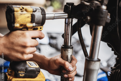 Mechanic using cordless impact wrench to disassemble motorcycle front fork and triple tree assembly
