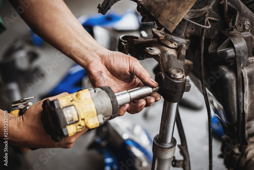 Mechanic using cordless impact wrench to disassemble motorcycle front fork and triple tree assembly