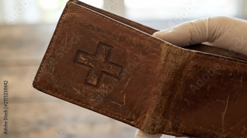 Healthcare wallet leather brown cross symbol spending innovation gloved hand holding worn pouch on rustic wooden table for medical cost concept