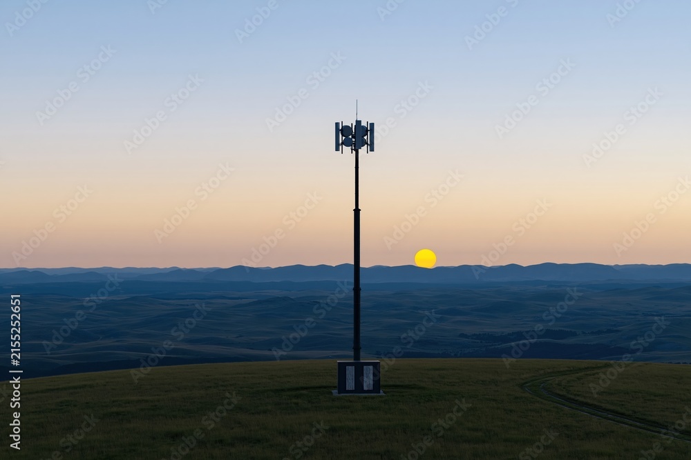Obraz premium Cellular communications mast on a grassy hill ridge at sunset, featuring weathered steel and a glowing amber sky for rural connectivity marketing