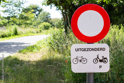 Road sign indicating no entry for vehicles except bicycles, featuring a red circle and bicycle icons, set against a green landscape with a pathway