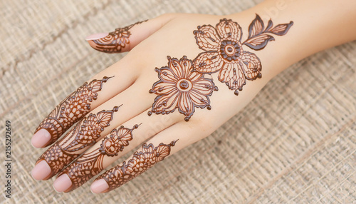 Intricate floral henna tattoo design on female hand and fingers, traditional mehndi art brown herbal pattern, ethnic temporary body paint on textured fabric background