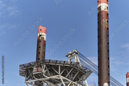 Esbjerg, Denmark - 29 July 2026: View of the Ziton Wind Enterprise crane ship heli platform with its prominent red and white support pillars against a clear blue sky.