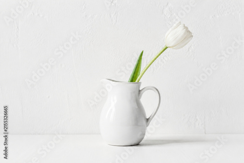 White ceramic milk pitcher with single tulip on white tabletop, minimalism and purity concept